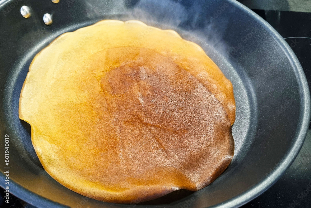 Large Golden Pancake Cooking on Black Non-Stick Frying Pan Large Golden Pancake Cooking on Black Non-Stick Frying Pan
