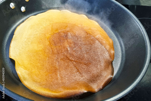 Large Golden Pancake Cooking on Black Non-Stick Frying Pan