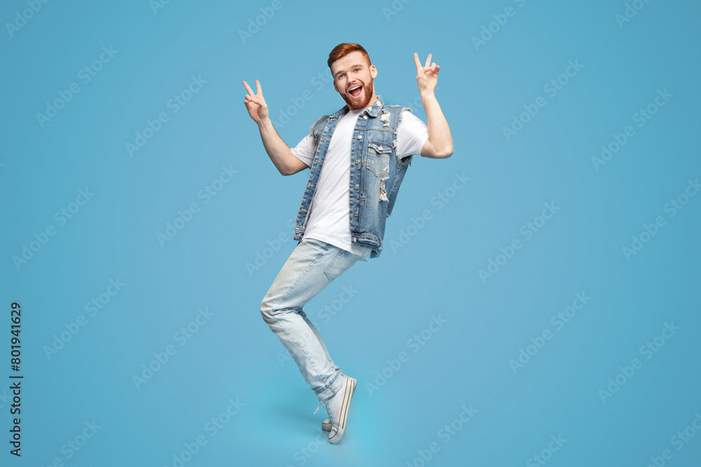 Awesome guy showing peace gesture and standing on tiptoes on blue background, copy space Awesome guy showing peace gesture and standing on tiptoes on blue background, copy space