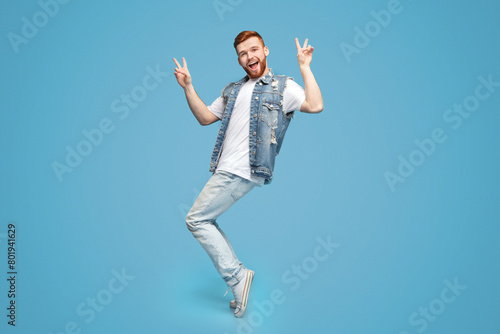 Awesome guy showing peace gesture and standing on tiptoes on blue background, copy space