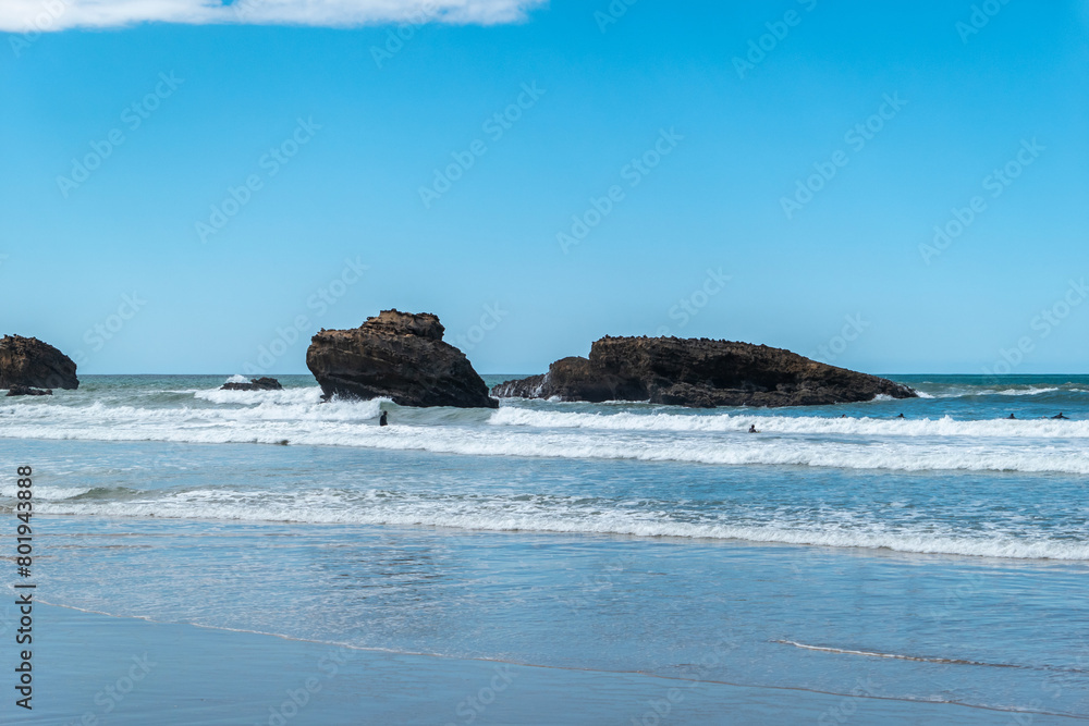 Praia com alguns rochedos e surfistas a desfrutarem das ondas sob um sol radiante no horizonte Praia com alguns rochedos e surfistas a desfrutarem das ondas sob um sol radiante no horizonte