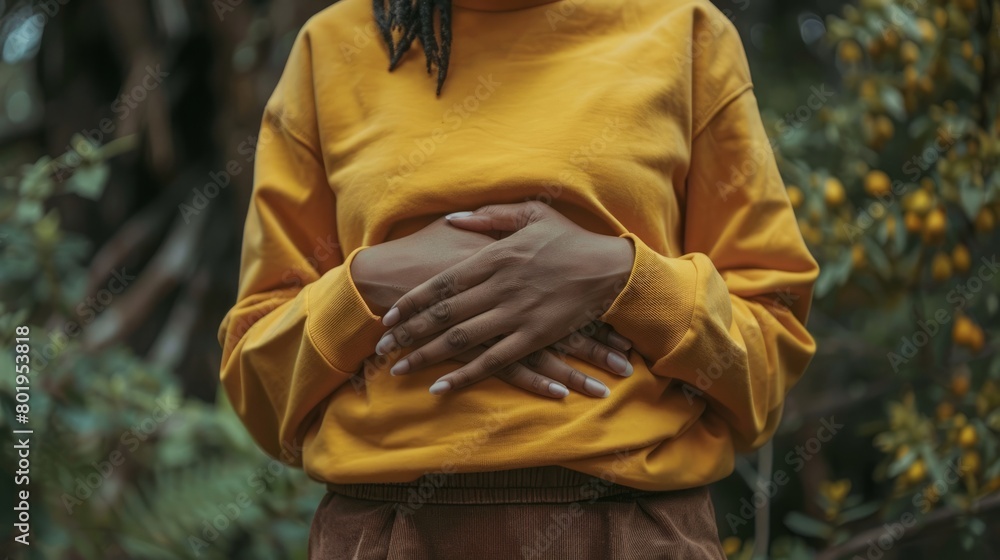 Fototapeta premium A person holding their abdomen with a pained expression, depicting symptoms of stomach ache or cramps associated with gastrointestinal issues.