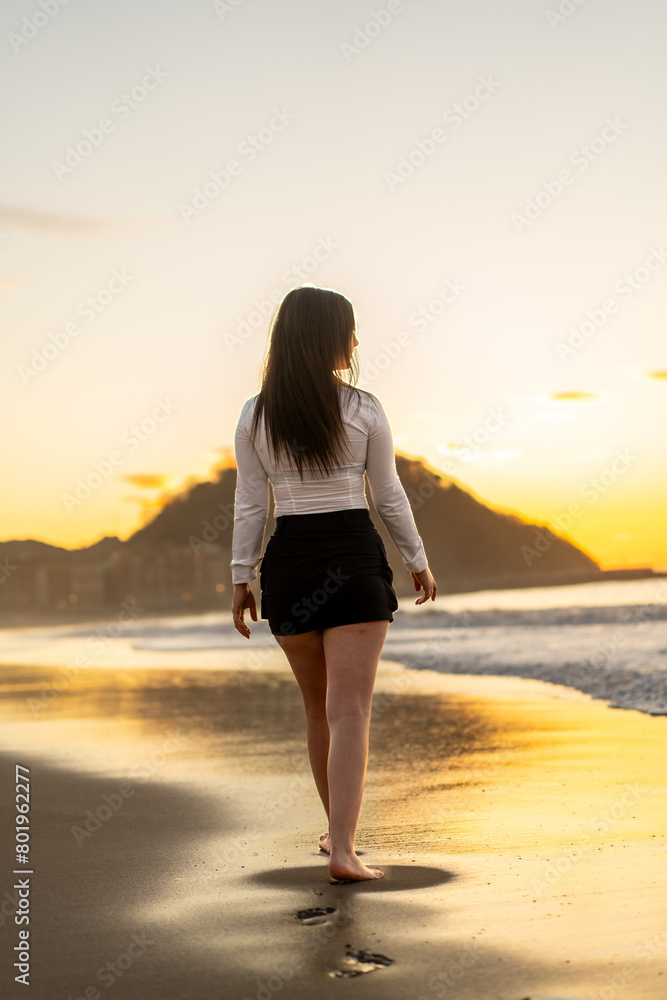 Woman walking barefoot along the beach during sunset