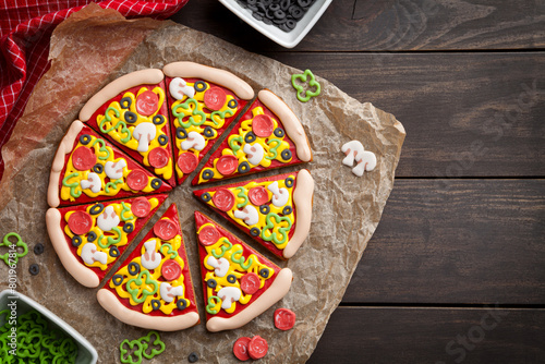 A creative display of gingerbread cookies, intricately decorated to resemble vibrant pizza slices, laid on parchment paper with candy toppings scattered around.