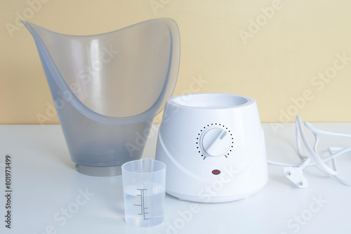 Facial steamer - white device on table with a container with water next to it
