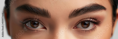 Highlight the elegance of artificial eyelashes and defined eyebrows through a sophisticated beauty composition, accentuating the model's features against a neutral background to em photo
