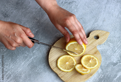 Female hands cut lemons on a wooden board on a gray background with space for text