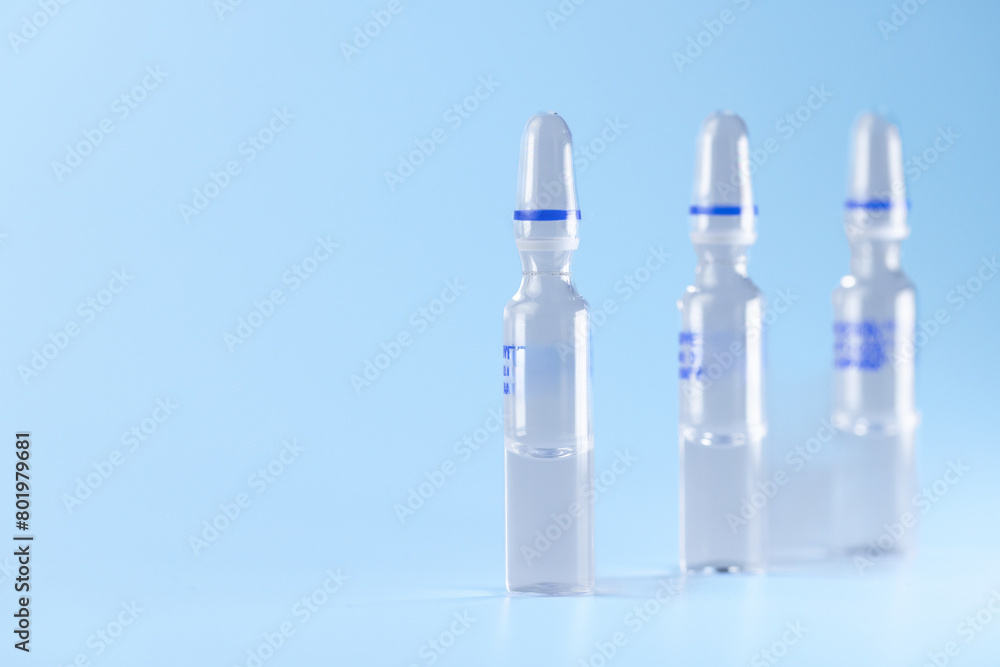 Three small bottles of medicine are lined up on a blue background. The bottles are clear and have blue stripes on them. Scene is calm and peaceful, as the bottles are not in use Three small bottles of medicine are lined up on a blue background. The bottles are clear and have blue stripes on them. Scene is calm and peaceful, as the bottles are not in use