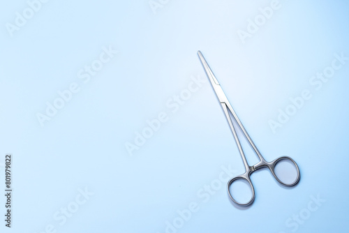 A pair of scissors is on a blue background. The scissors are silver and have a pointed tip. Concept of precision and focus, as the scissors are a tool used for cutting and shaping