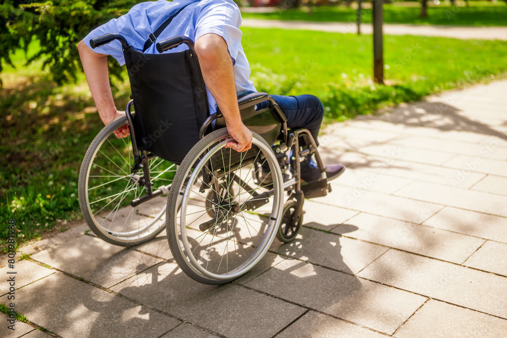 Naklejka premium Close up image of man in wheelchair rolling on pathway in park.