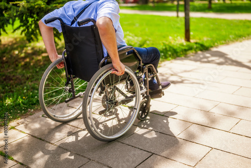 Close up image of man in wheelchair rolling on pathway in park. photo