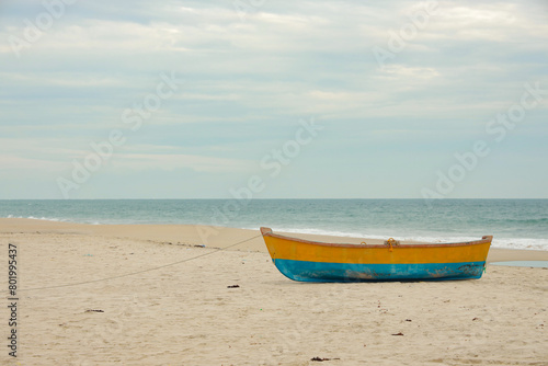 Traditional Wooden fishing boat in blue and yellow colors on white sand beach in Ghost Town near to Dhanushkodi beach