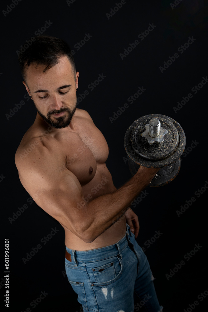 Strong shirtless man doing biceps with dumbbell in photo studio Strong shirtless man doing biceps with dumbbell in photo studio