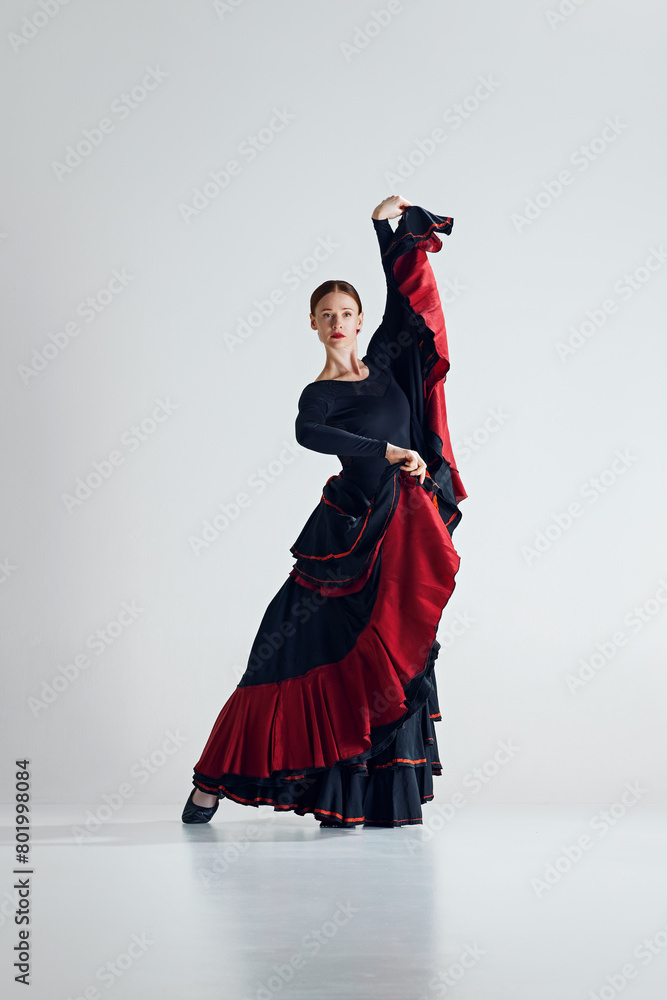 Elegance in motion. Skilled flamenco dancer, beautiful woman in expressive dress performing, dancing against grey studio background. Concept of art of movement, classical dance, beauty Elegance in motion. Skilled flamenco dancer, beautiful woman in expressive dress performing, dancing against grey studio background. Concept of art of movement, classical dance, beauty