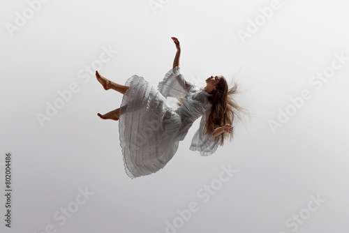 Photography Woman in white ruffled dress floats effortlessly in moment of graceful falling in mid-air against white studio background
