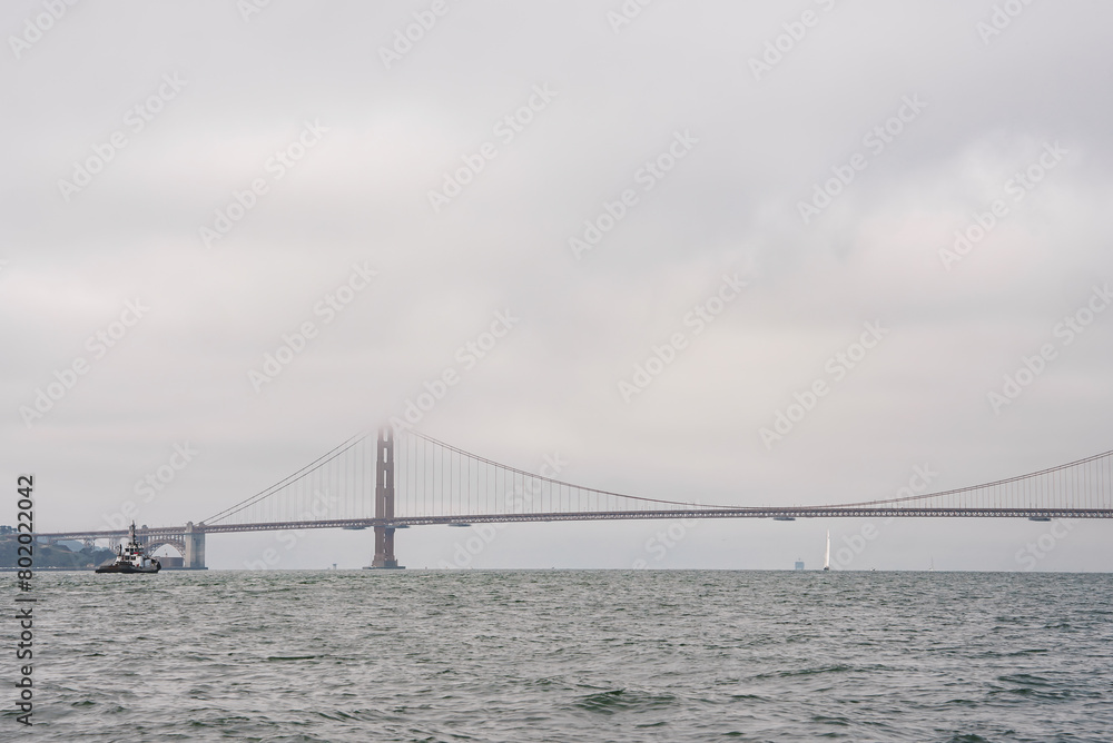 Tranquil view of Golden Gate Bridge in San Francisco, CA. Overcast sky, calm water, boat for scale. Serene simplicity of iconic bridge against muted colors.