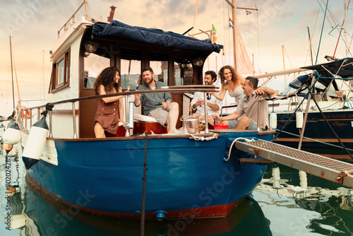Friends share drinks and laughs on a classic boat at sunset, creating a picturesque and relaxed social scene in the marina. (ID: 802024285)