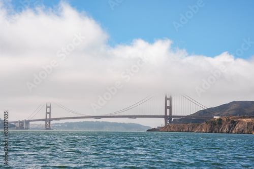 Daytime view of the Golden Gate Bridge in San Francisco  CA. Iconic orange bridge against blue sky  serene water  suspension towers  Marin Headlands frame landscape. Tranquil and majestic scene.