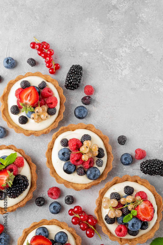 Tartlets with custard vanilla cream with fresh berries and mint on a gray concrete background. Summer dessert. Tartlets with custard vanilla cream with fresh berries and mint on a gray concrete background. Summer dessert.