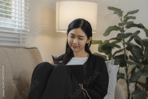 the girl teenaeger is sitting on the cozy couch in the living room of her apartment and spending a free time on what her interasted, sitting happily on the comfrotable sofa photo