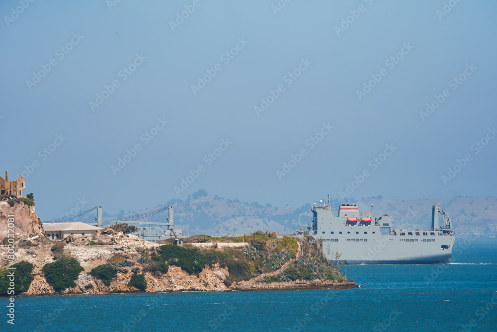 Scenic view of Alcatraz Island in San Francisco Bay with a cargo ship passing by, hinting at its historical past as a federal prison and military facility.