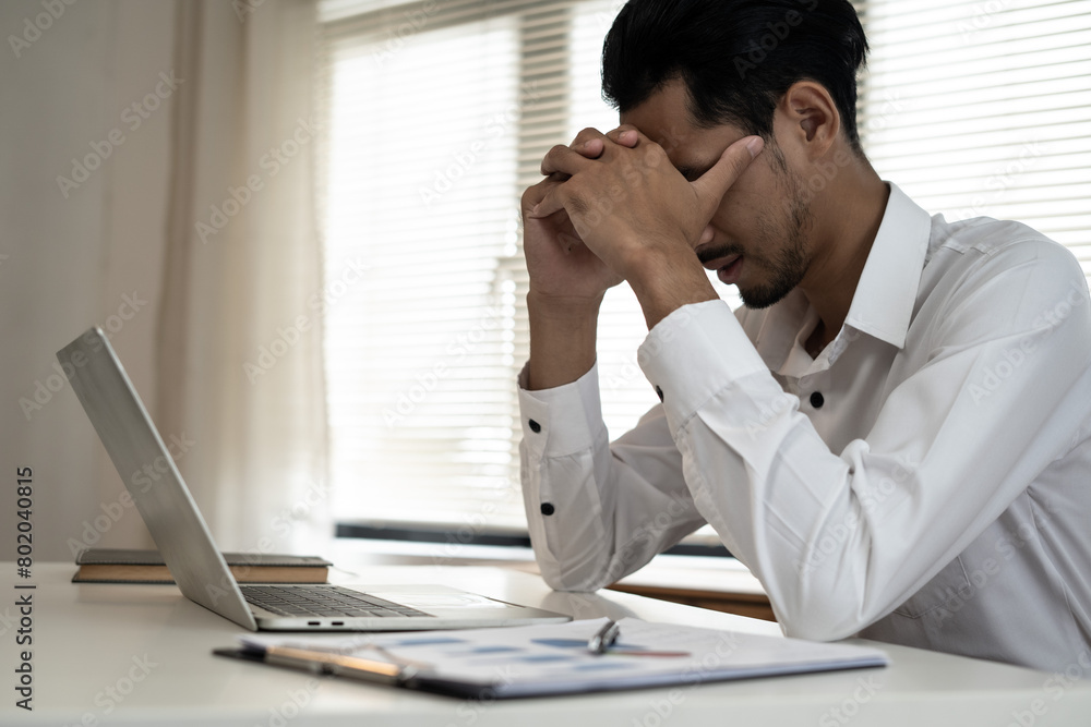Asian businessman massaging his nose and keeping eyes closed while thinking about financial problems with feeling stressed and tired between work day Asian businessman massaging his nose and keeping eyes closed while thinking about financial problems with feeling stressed and tired between work day