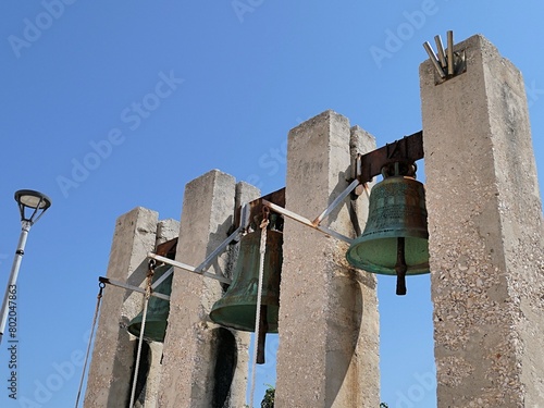 Outdoor three massive church bells on concrete columns in front of catholic Church of Our Lady Of The Rosary in Razanac, northern Dalmatia, Croatia, sunlit by august summer sunshine.