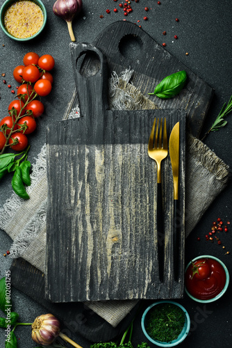 Creative kitchen banner. Cutting board, cutlery, spices and kitchen utensils on black stone background. Free space for text.