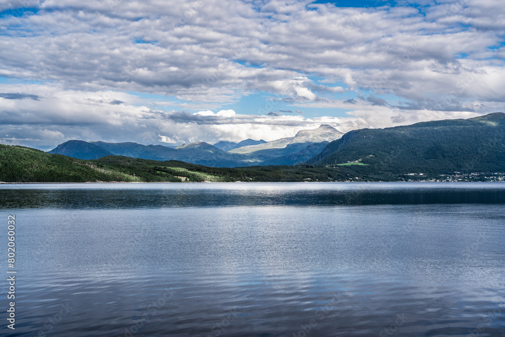 Overlooking the flat, calm waters of the Ålvundfjord. View of the other side of the fjord coastline with the village of Handlarstuhamran against the backdrop of the Trollheimen Mountains in Norway. Overlooking the flat, calm waters of the Ålvundfjord. View of the other side of the fjord coastline with the village of Handlarstuhamran against the backdrop of the Trollheimen Mountains in Norway.