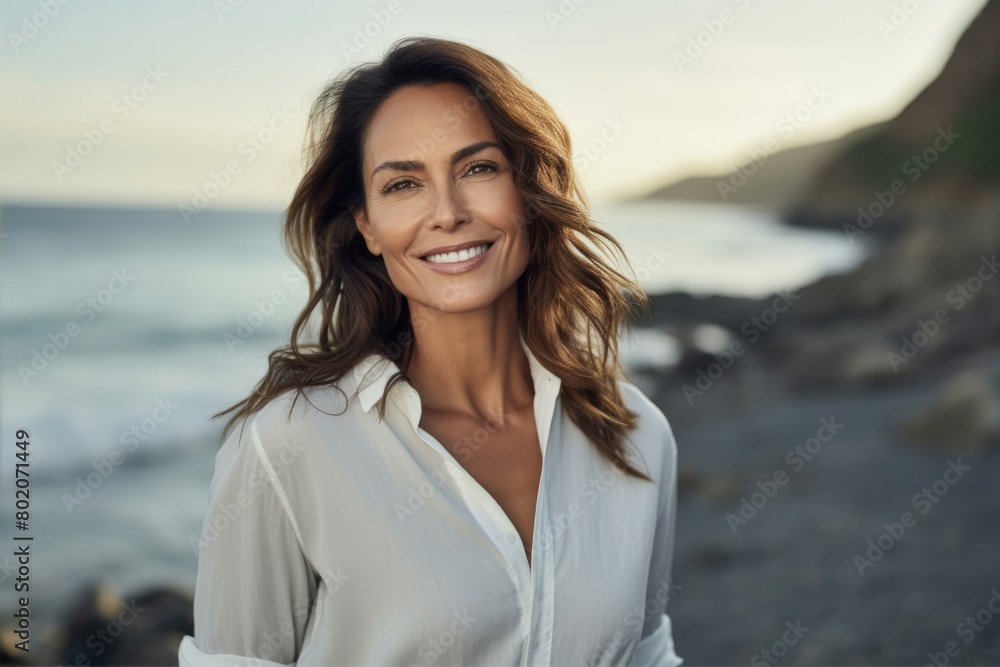 Caucasian woman in her 40th smiling in white shirt by the sea, lifestyle and health themes.