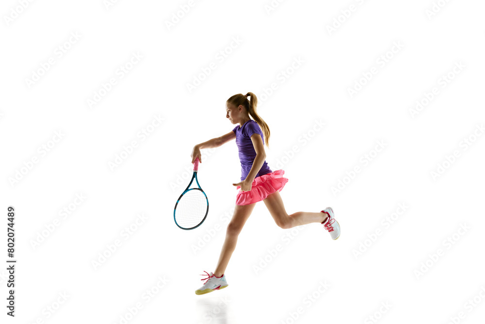 Portrait of young sportive girl, teenage tennis player in uniform training in motion against white studio background. Concept of professional sport, movement, tournament, action. Ad