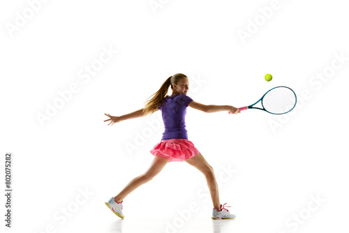 Sportive young girl, tennis athlete in comfortable vibrant uniform playing tennis in motion against white studio background. Concept of professional sport, movement, tournament, action. Ad © Lustre
