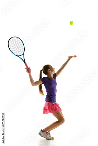 Concentration. Teenage athlete girl, tennis player perfectly serving ball in motion to opponent against white studio background. Concept of professional sport, movement, tournament, action. Ad