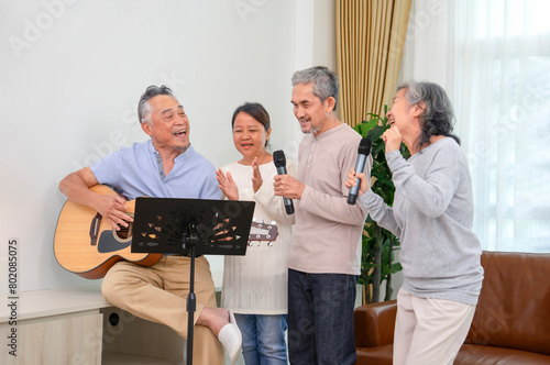 group of asian friends meetup at home,playing guitar and singing a song together joyfully in the living room,concept of aging society,friendship,entertainment,recreation