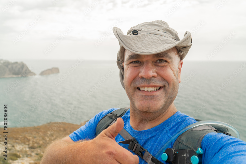 Smiling hiker with a hat takes a selfie on a cliff 