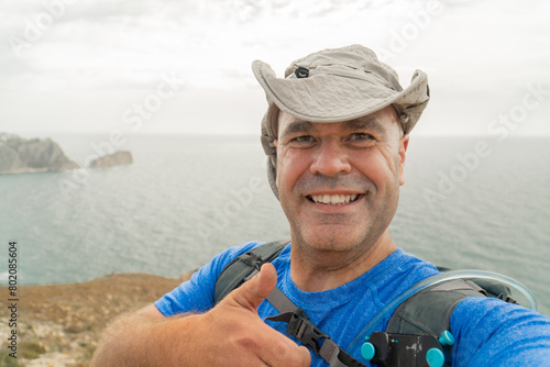 Smiling hiker with a hat takes a selfie on a cliff 