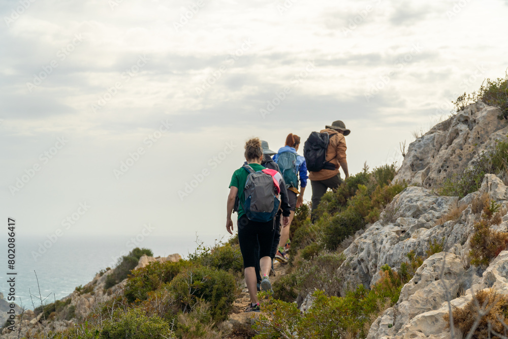 Fototapeta premium Unrecognizables hikers in a row, walking on the rocks, the sea is on the background.