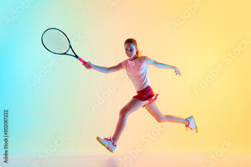 Portrait of young girl, teen tennis player in uniform training hitting ball in neon light against blue-yellow background. Concept of individual kind of sports, fashion, tournament, action. Ad © Lustre