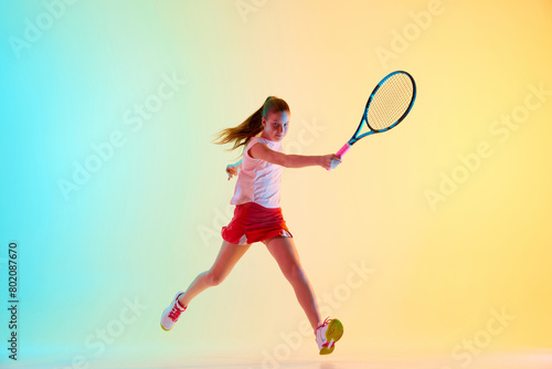 Young tennis player leaps into action , her racket poised to strike a powerful forehand shot in neon light against blue-yellow background. Concept of individual kind of sports, fashion, tournament.
