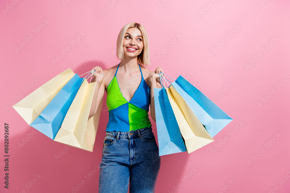 Photo of positive girl with bob hair dressed colorful tank holding new clothes in bags look empty space isolated on pink color background