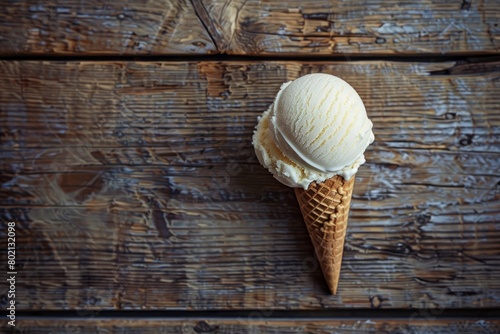 Top-down view of an ice cream scoop nestled in a waffle cone on a rustic wooden surface © Ilia Nesolenyi