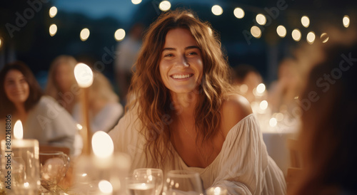 An attractive woman smiling at the camera while sitting next to friends during an outdoor dinner party