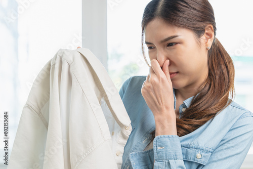 Slika na platnu Smelly clothes laundry, housewife woman having bad smelling clothes on the hand holding breath nose with finger, sniff smelly dirty stinky musty and look disgusting