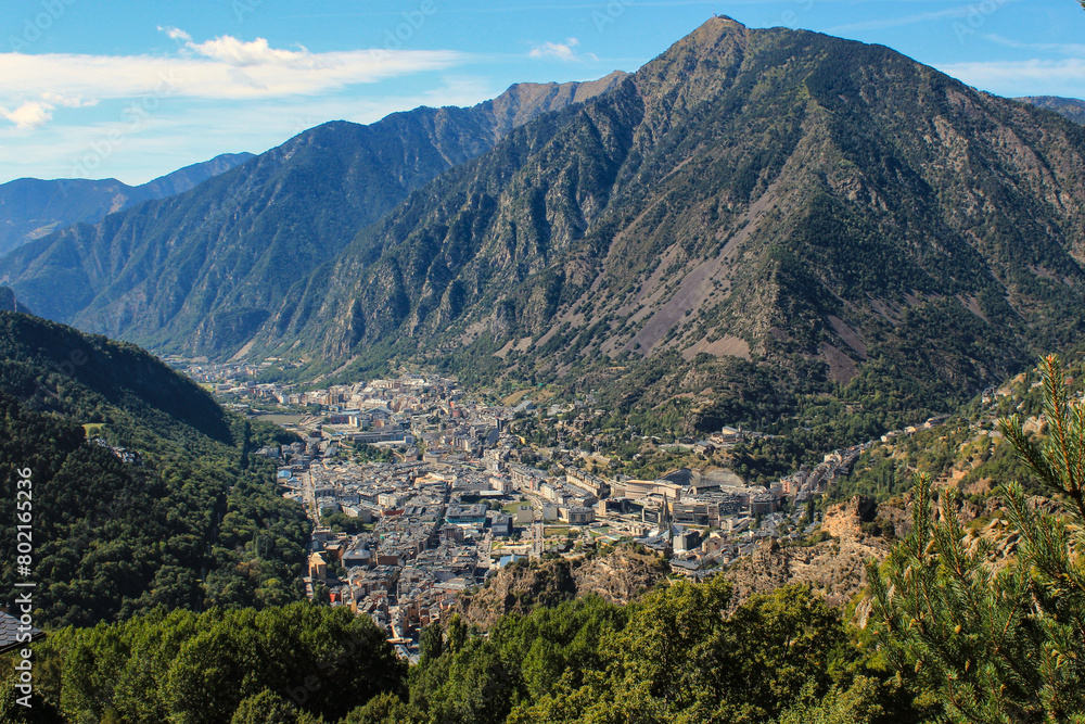 The city is surrounded by mountains against a background of blue sky from a bird's eye view, Andorra.