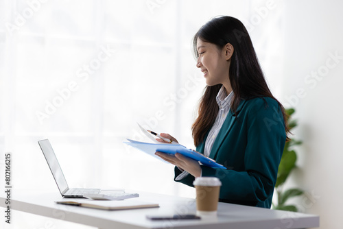Beautiful Asian businesswoman working with laptop and paperwork on desk in office.