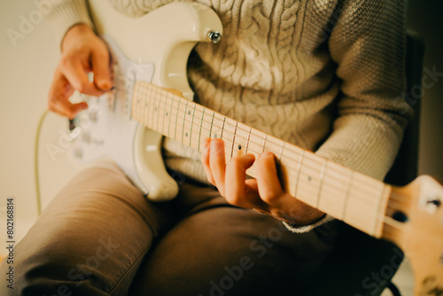 A man wearing a white sweater is playing music on a white electric guitar during a music lesson. photo