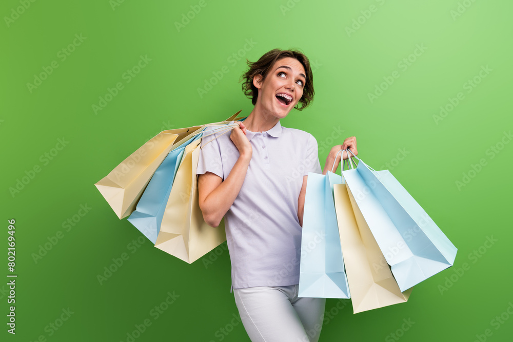 Photo of laugh joke young girl after shopping center bring bags home lookin empty space more discounts isolated on green color background Photo of laugh joke young girl after shopping center bring bags home lookin empty space more discounts isolated on green color background