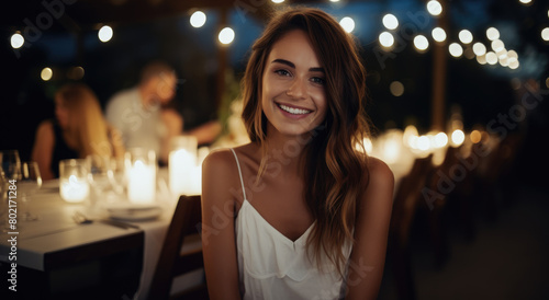 An attractive woman smiling at the camera while sitting next to friends during an outdoor dinner party