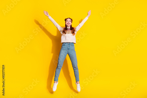 Photo portrait of attractive woman jump raise hands excited dressed stylish knitted warm outfit isolated on yellow color background