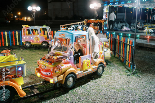 Little girl sits in a children train carriage at a fair photo